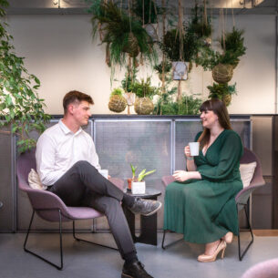 A man and a woman sat in casual chairs having coffee and a conversation.