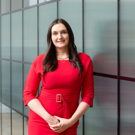 Woman in a red dress leaning against a glass partition wall.